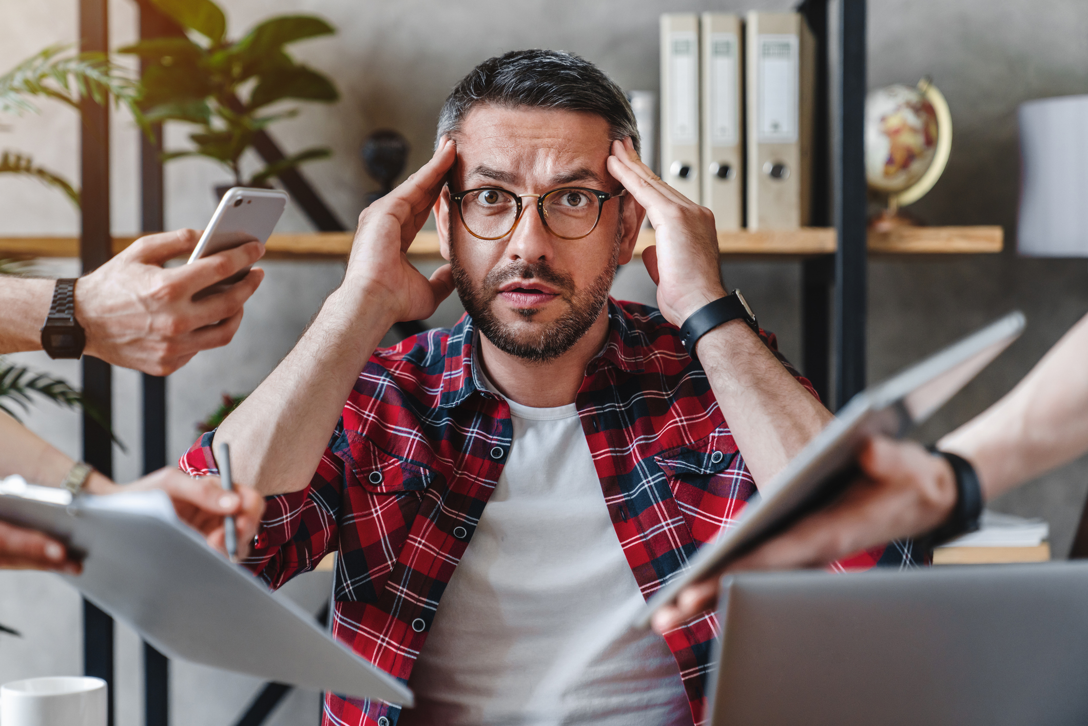 Photo of an overworked businessman sitting at laptop overloaded with work multiple tasks in modern office.