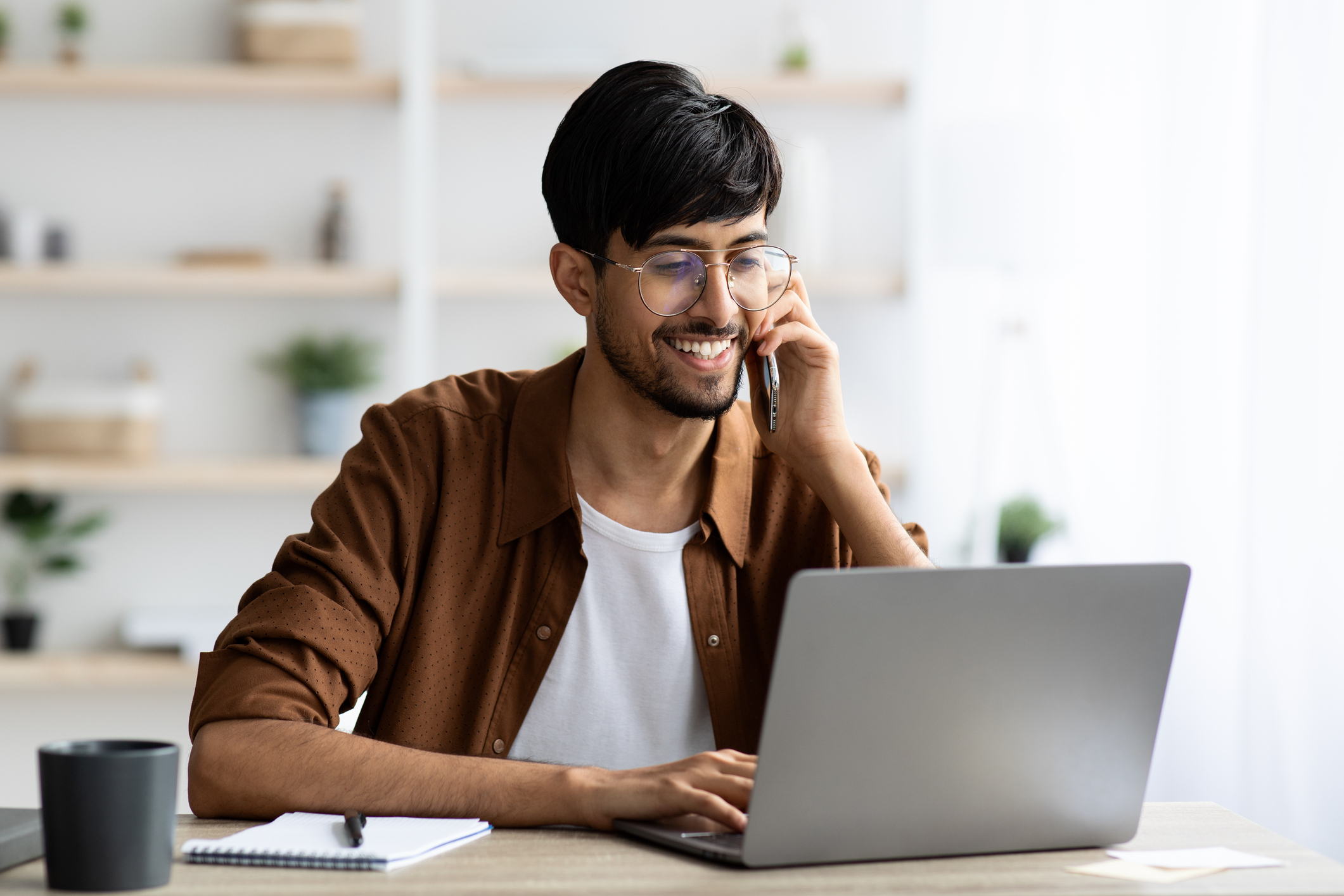 Photo of a cheerful man on a phone and looking at a computer