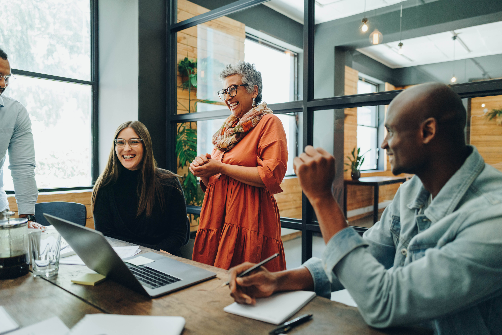 GettyImages-1395144844 Photo of Diverse businesspeople smiling cheerfully during a meeting in a modern office.