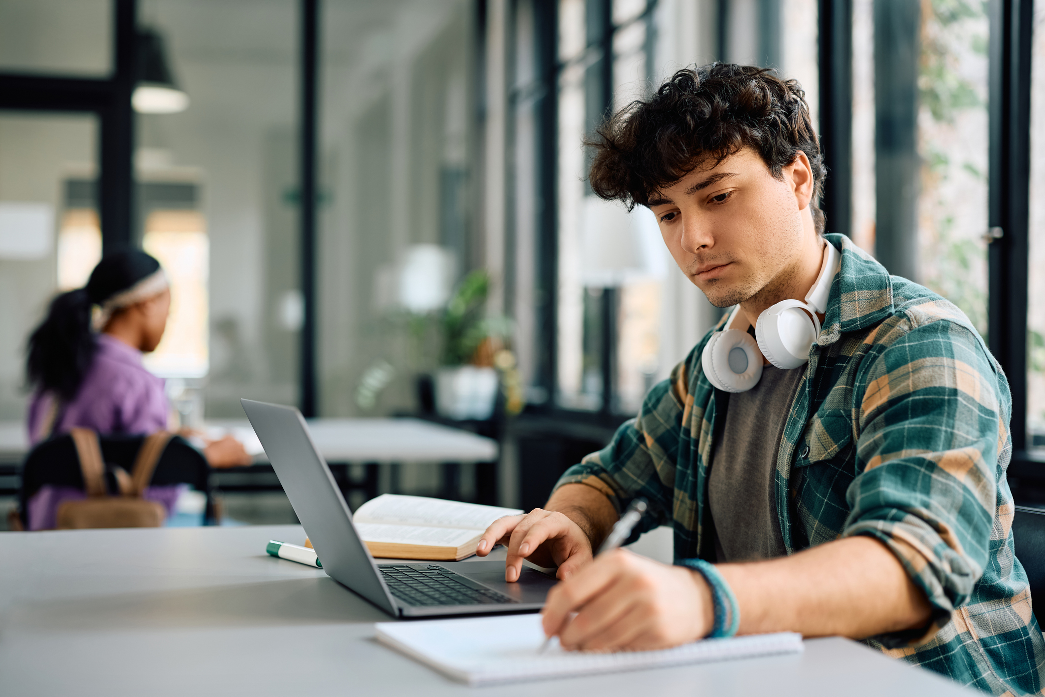 Photo of University student writing while using laptop and studying in the classroom.