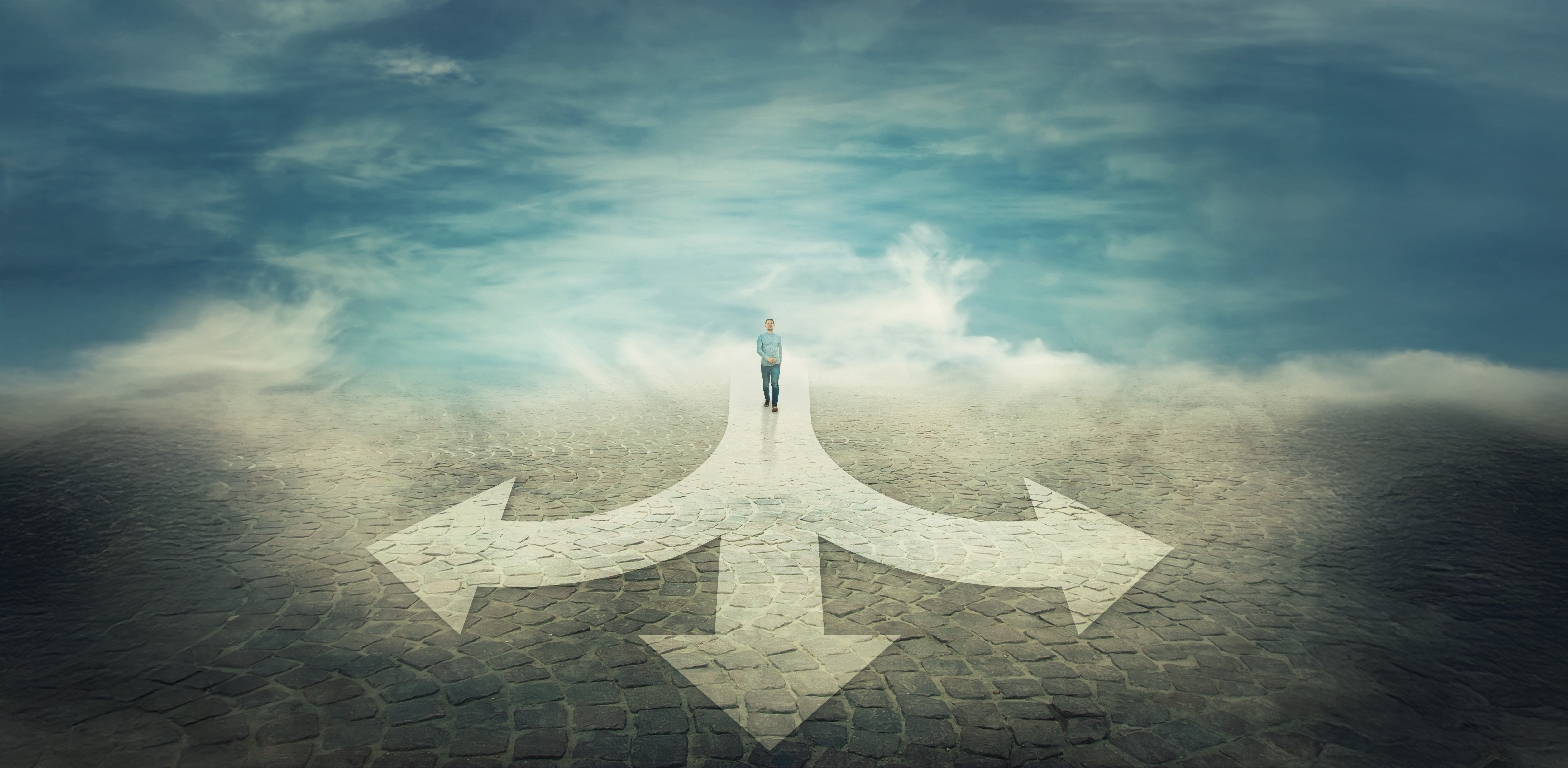 GettyImages-1067297034 Surreal view as a man walking in front of a crossroad where road is splitted in three different ways as arrows